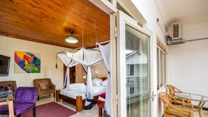A bedroom with a bed, a chair, a table, and a glass door leading to a balcony. - 2 Friends Beach Hotel (Entebbe)