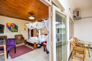 A bedroom with a bed, a chair, a table, and a glass door leading to a balcony.