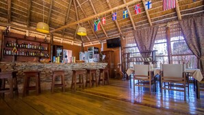 A rustic bar area with wooden stools, a stone counter, and flags hanging from the ceiling. - 2 Friends Guest House (Jinja)