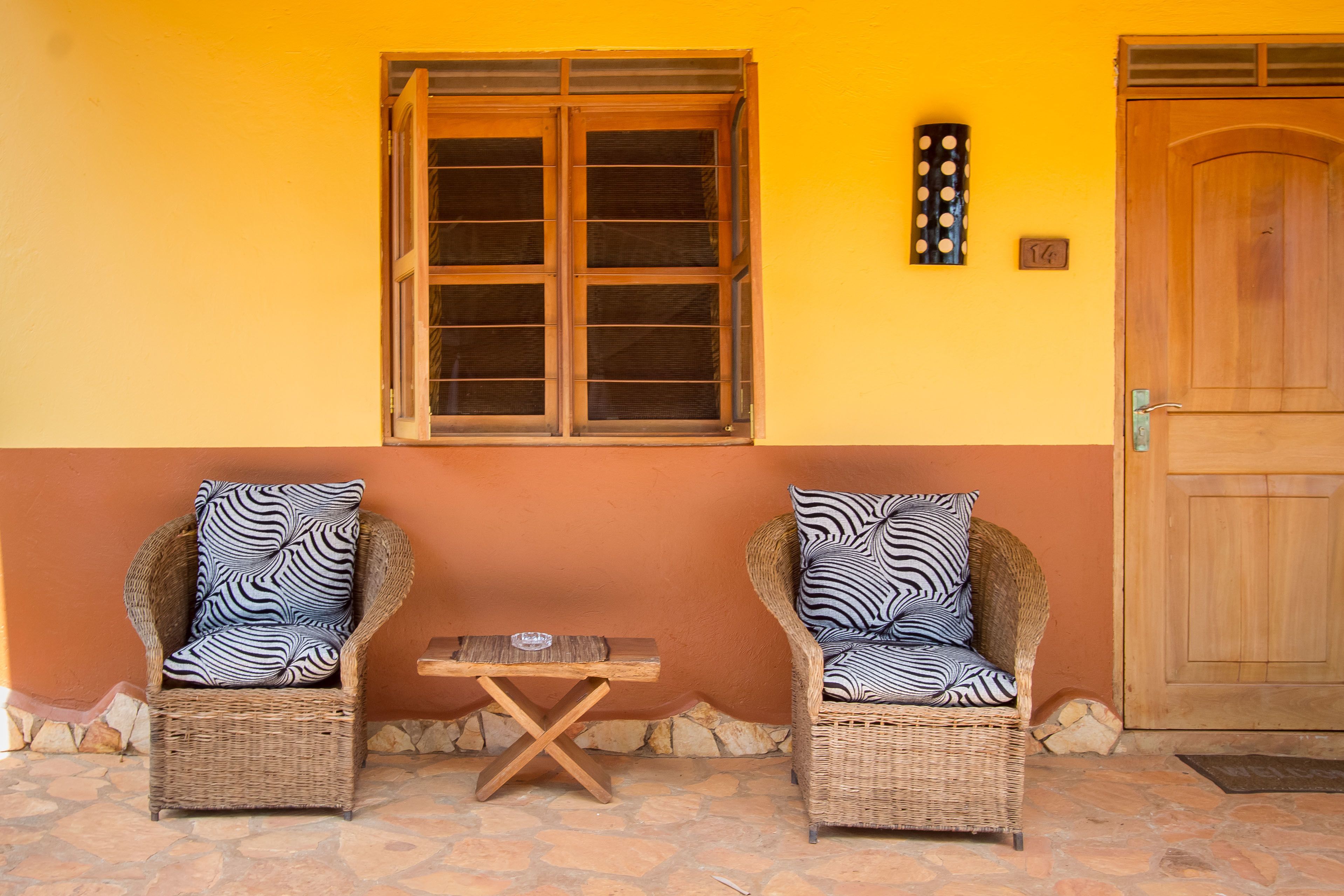 Two wicker chairs with patterned cushions, a small wooden table, and a window with a wooden frame.