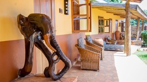 A sculpture of an elephant on a stone platform, wicker furniture, and a stone-tiled patio. - 2 Friends Guest House (Jinja)