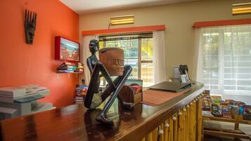 A reception area with a wooden counter, a sculpture, a poster, and a window with curtains.