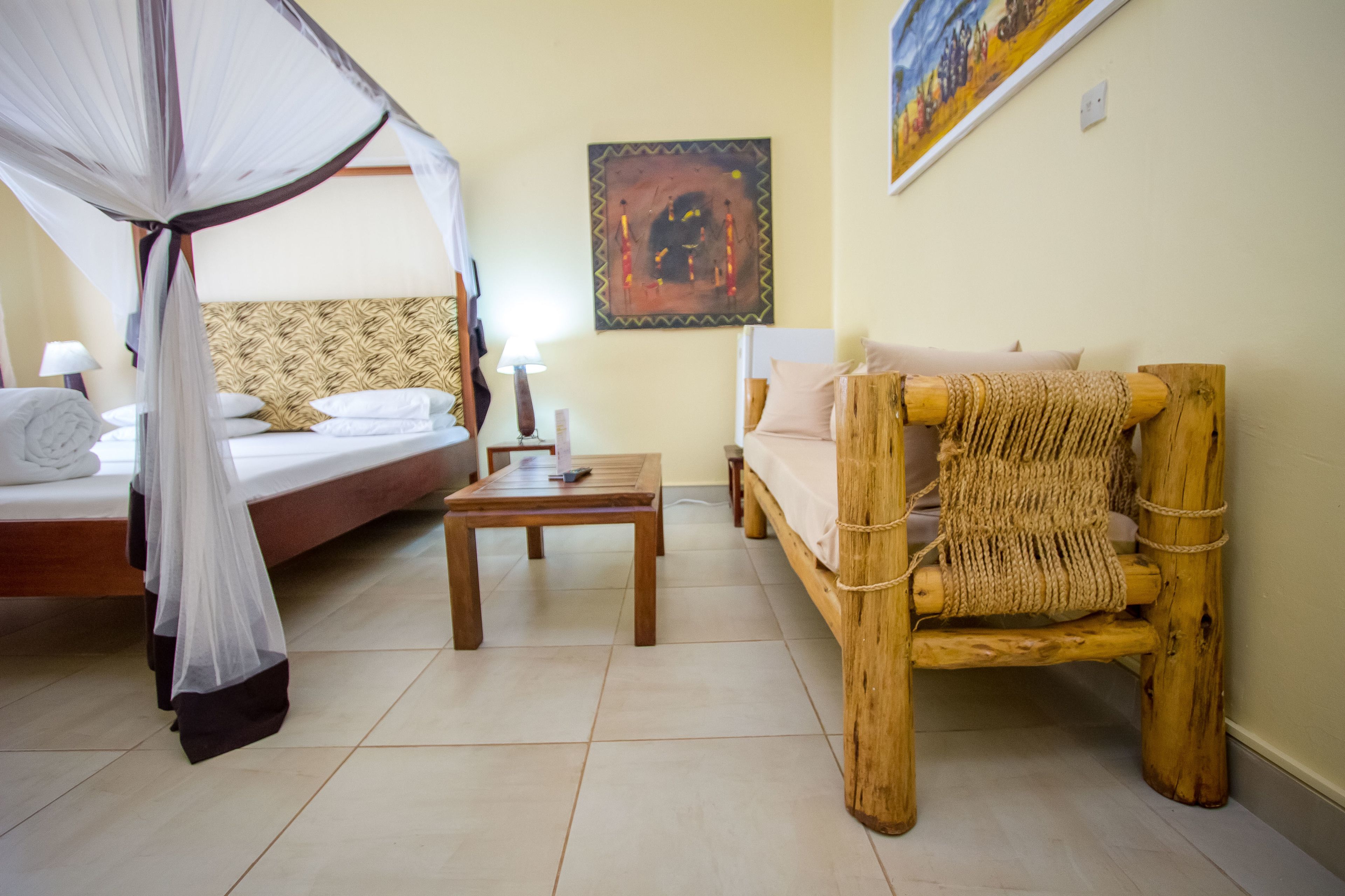 A room with a bed, a wooden chair, a table, and a wall painting.