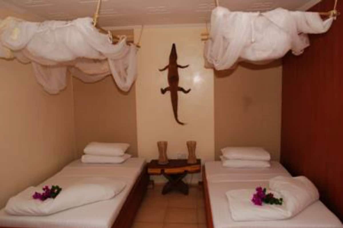 A room with two beds, each with a white bedspread and pillows, and a small table with a decorative item between them.