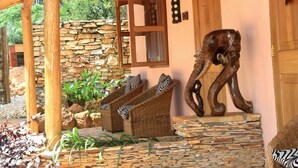 A rustic outdoor area with a stone wall, wooden furniture, and a wooden sculpture. - 2 Friends Guest House (Jinja)
