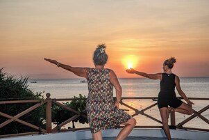 Dos personas en un balcón con vista al atardecer sobre el océano.