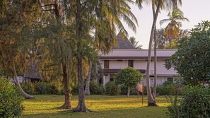 A house with a thatched roof, surrounded by lush greenery and palm trees. - Flame Tree Cottages (Nungwi)