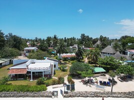 A coastal resort with multiple bungalow-style buildings, a sandy beach area with sun loungers, and lush greenery.