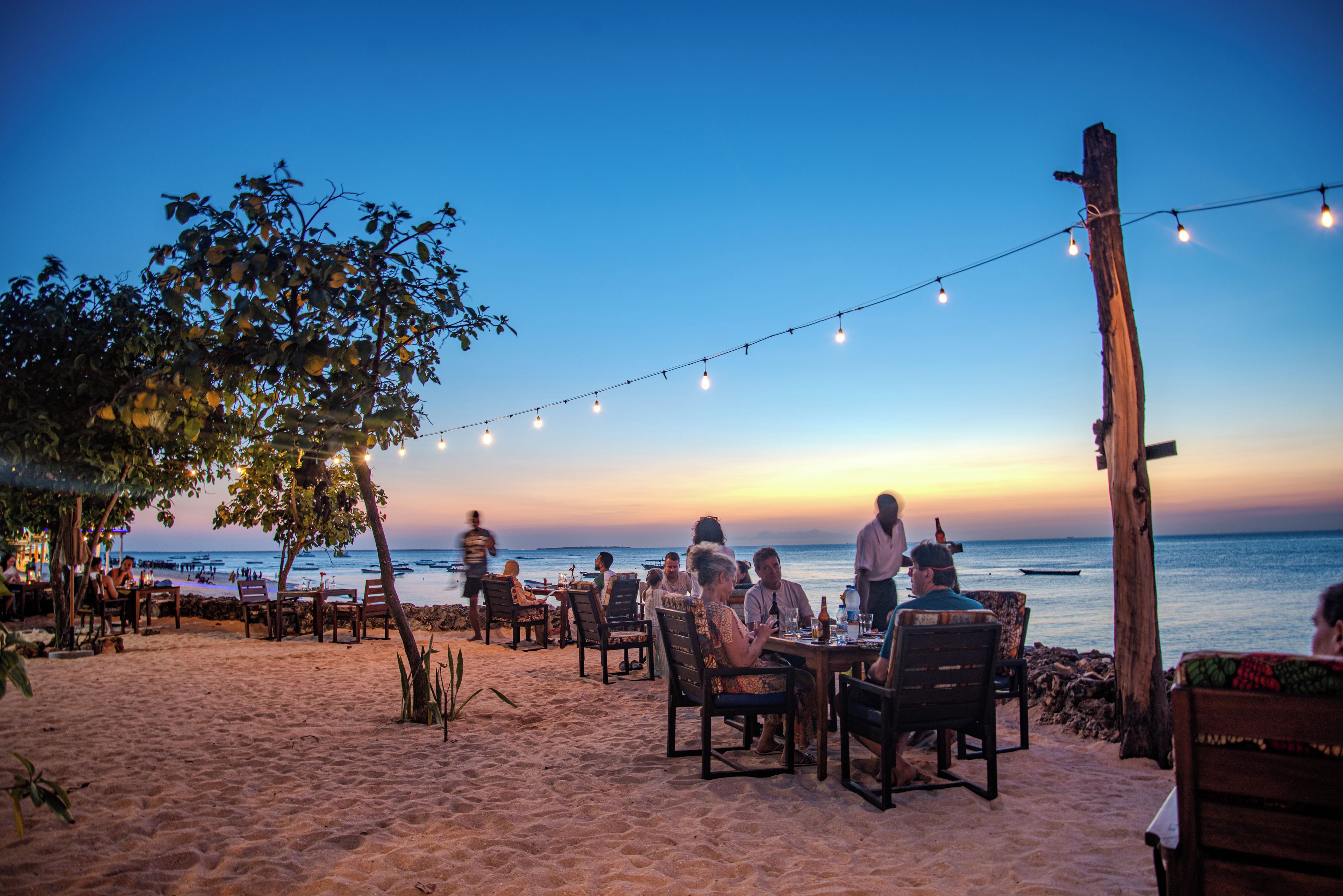 Un espace extérieur aménagé avec des tables et des chaises, offrant une vue sur une plage et l’océan.