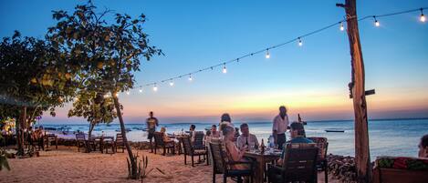 Un espace extérieur aménagé avec des tables et des chaises, offrant une vue sur une plage et l’océan.