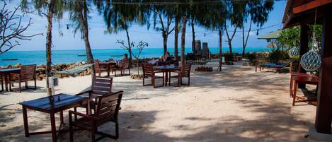 A beachside patio with wooden tables and chairs, overlooking the ocean.
