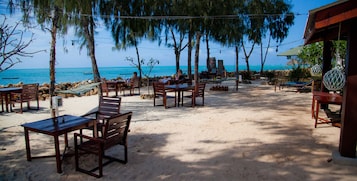 Un patio frente a la playa con mesas y sillas de madera, con vistas al océano.