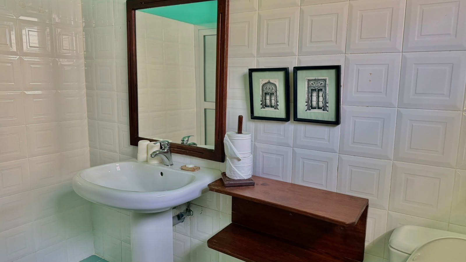 Un bagno con un lavandino bianco, uno specchio e due quadri appesi al muro.