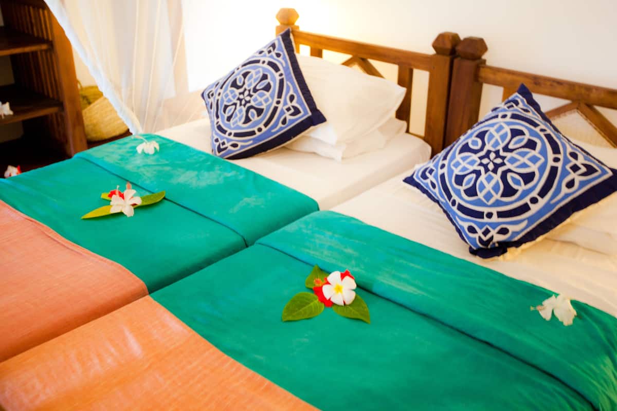 Una cama con dos sábanas verdes, almohadas blancas y almohadones con diseños azules.