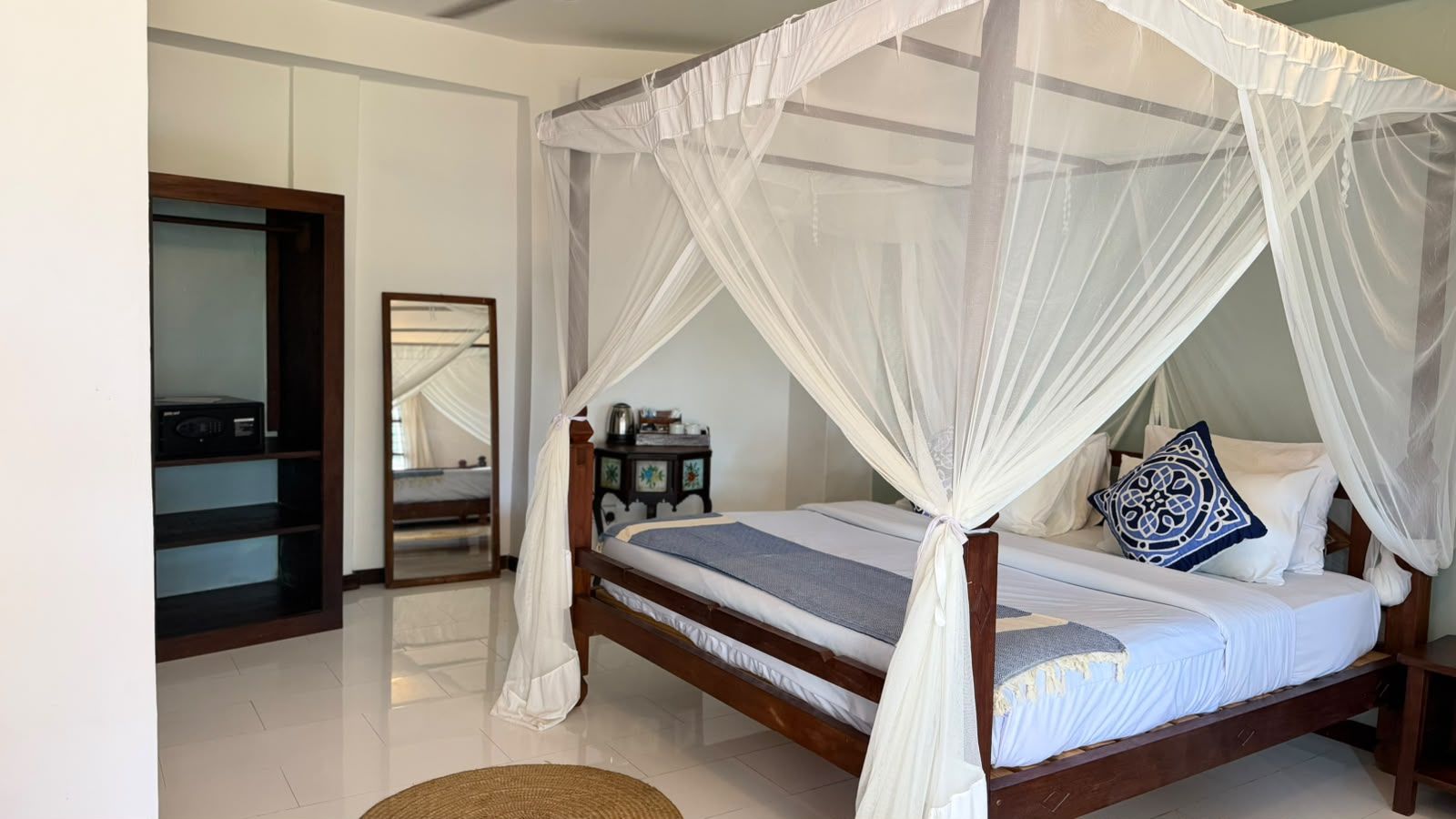 A bedroom with a four-poster bed, a bedside table, and a mirror.