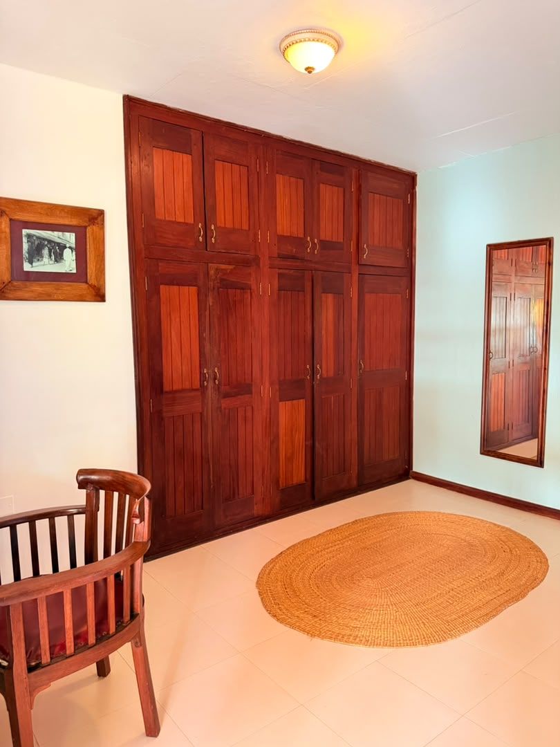 A room with a large wooden wardrobe, a woven rug, and a wooden chair.