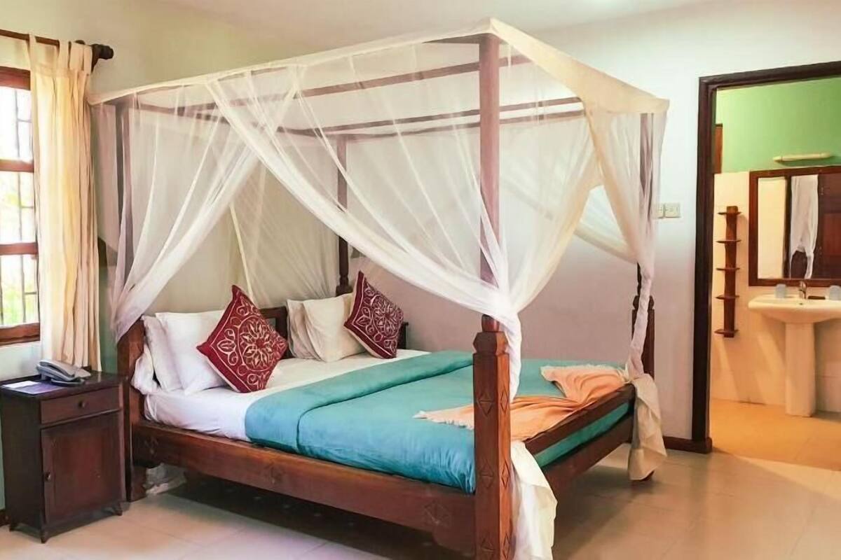 Una cama con dosel, una mesita de noche, un tocador y un baño con lavamanos y espejo.
