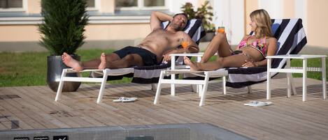 A poolside area with lounge chairs and a hot tub.