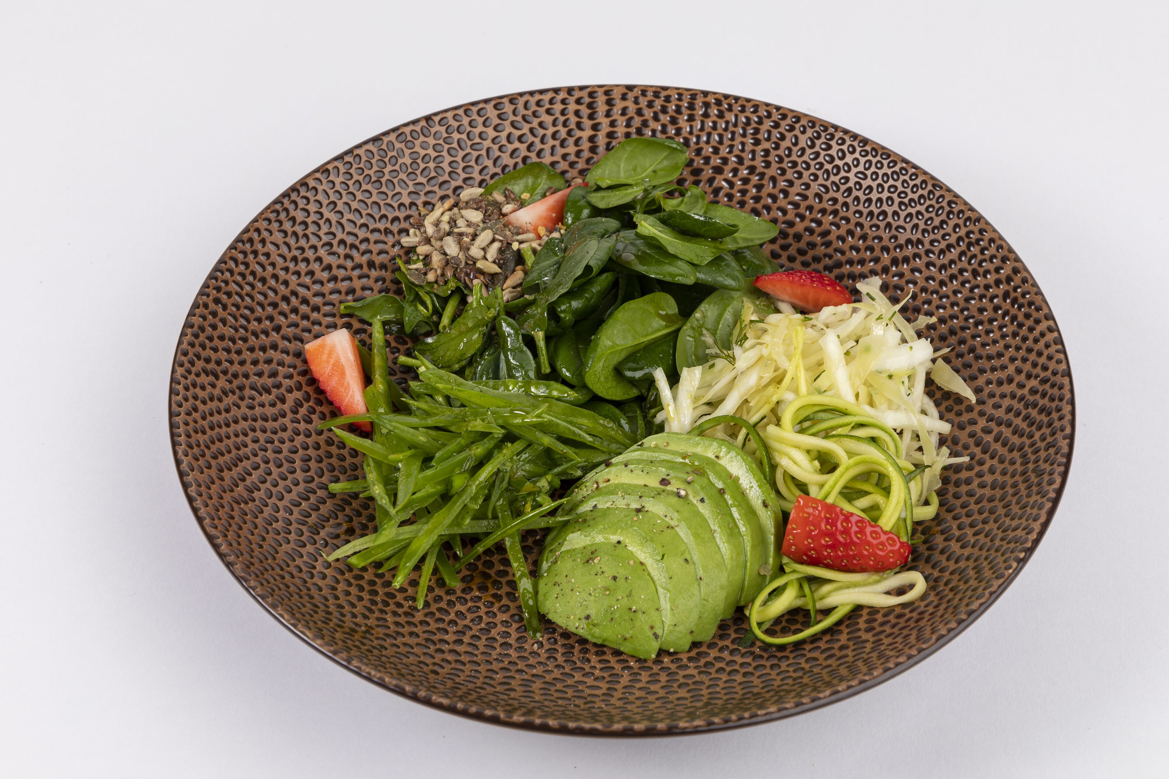 A plate with various vegetables including spinach, zucchini, and sliced avocado.