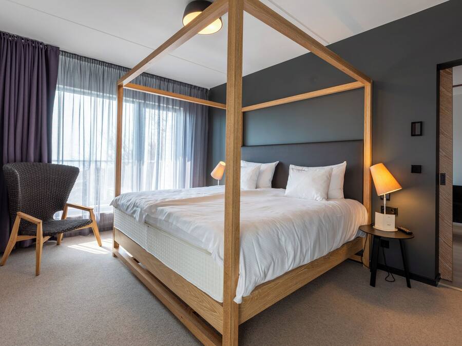Una cama con dosel en una habitación de hotel, con una silla y una mesita de noche.