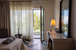 Une chambre d’hôtel avec un lit, un bureau avec une lampe, un grand miroir et une vue sur l’extérieur.