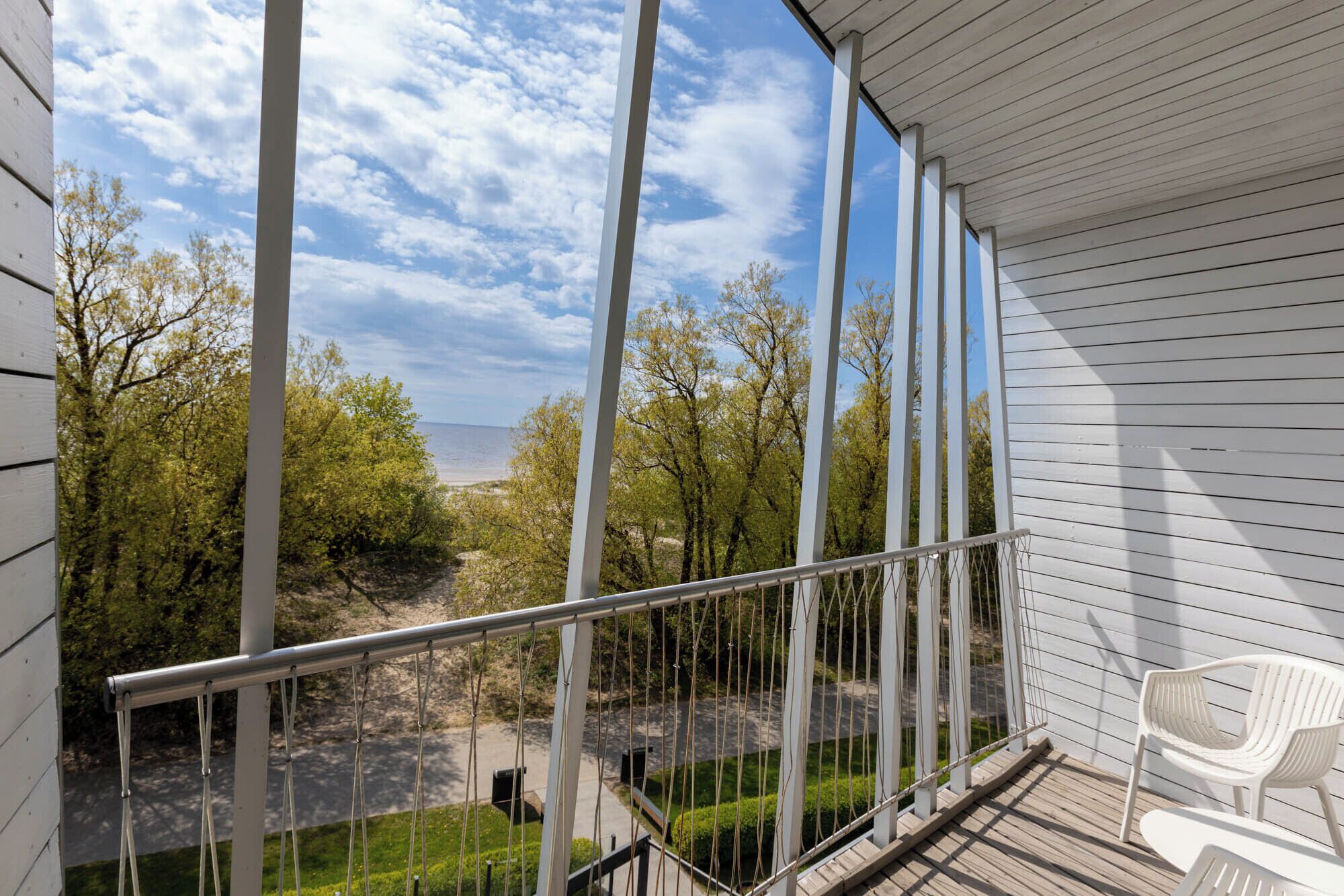 Ein Balkon mit Metallgeländer, der auf eine angelegte Grünfläche mit Bäumen und Meerblick führt.