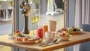 A dining table with plates of food, glasses of wine, a vase with flowers, and a bowl of fruit. - Hedon SPA & Hotel (Parnu)