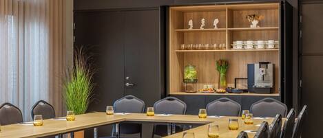 A conference room with a long table, chairs, a coffee station, and a decorative shelf with items.