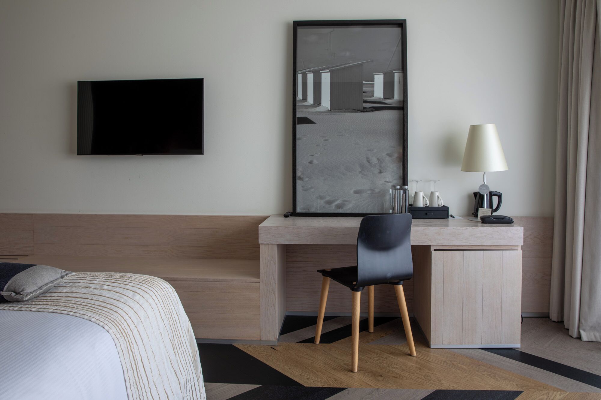 A hotel room with a bed, a desk with a chair, a television, a mirror, a lamp, and a coffee maker.