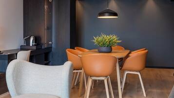 A modern dining area with a round table, six chairs, a potted plant, and a pendant light.