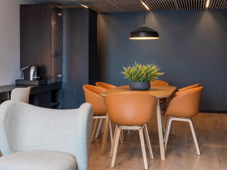 A modern dining area with a round table, six chairs, a potted plant, and a pendant light.