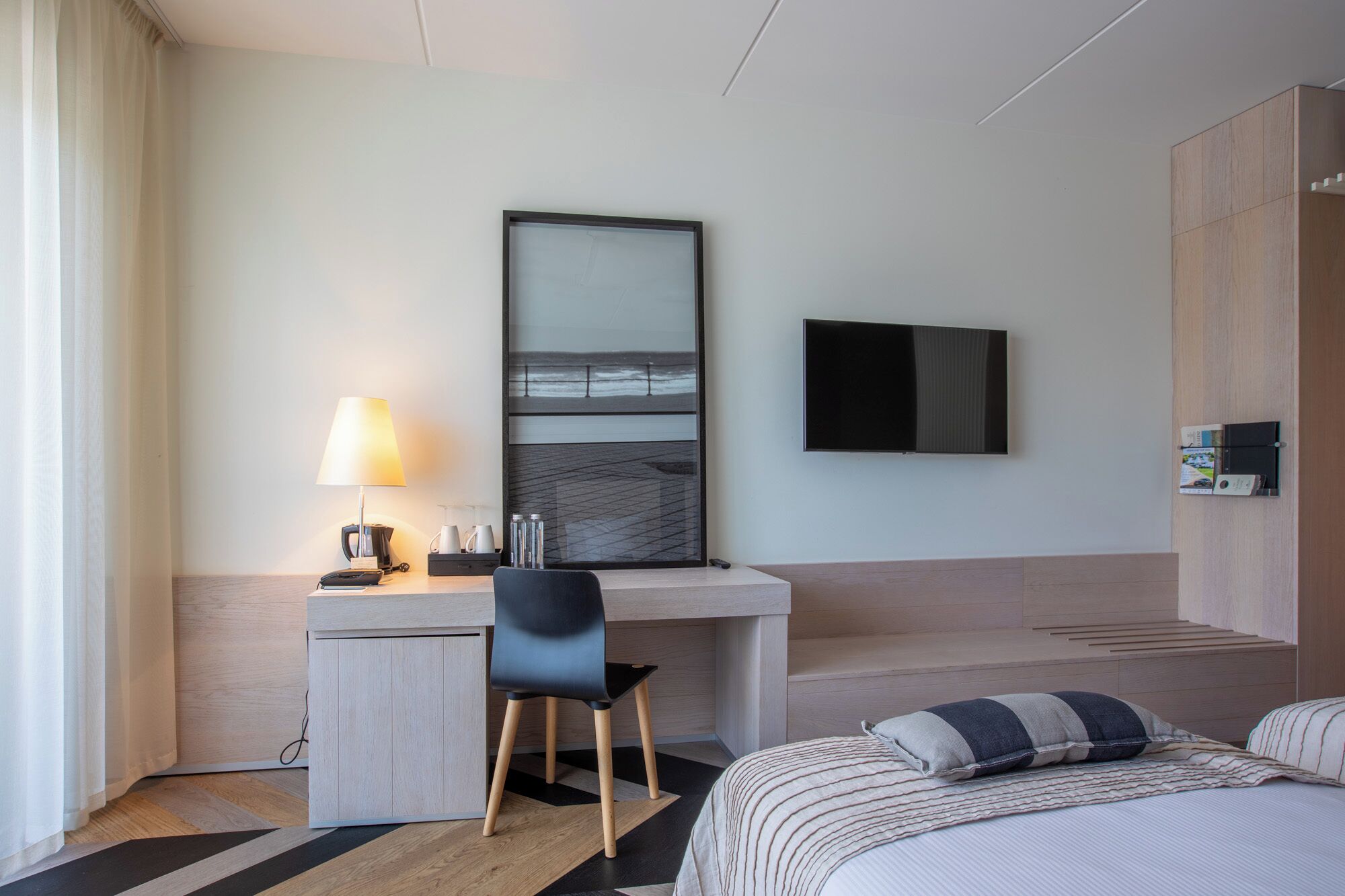 A hotel room with a desk, chair, bed, TV, and a large mirror.