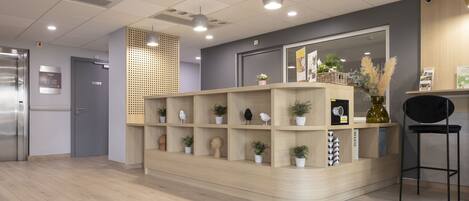 Zona de recepción con mostrador de madera, plantas en macetas y una silla negra.