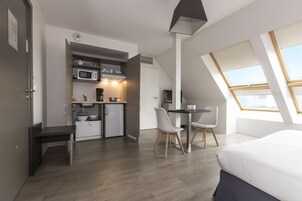 A compact room with a kitchenette, a dining area, and a bed.