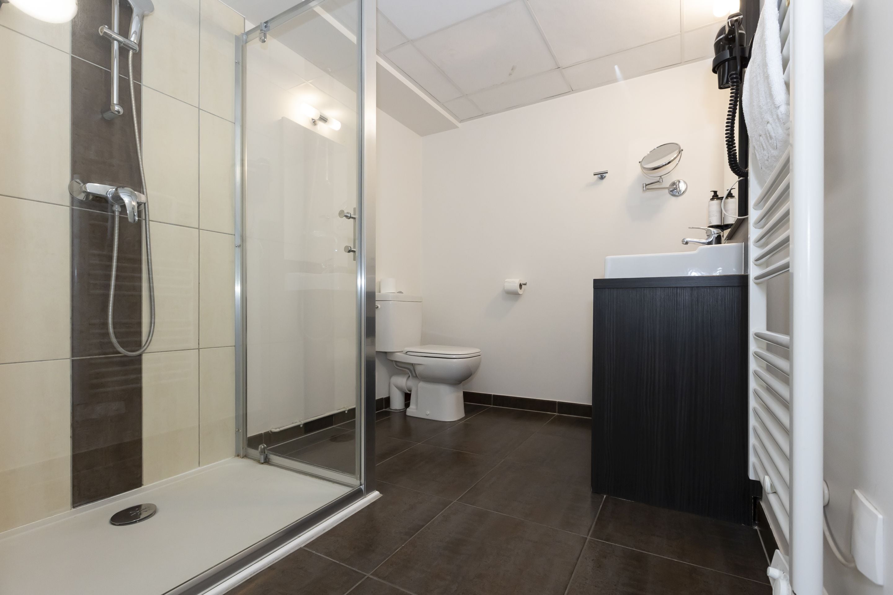 Un bagno moderno con cabina doccia in vetro, un water bianco e una zona lavandino dai toni scuri.
