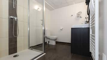 Un bagno moderno con cabina doccia in vetro, un water bianco e una zona lavandino dai toni scuri.