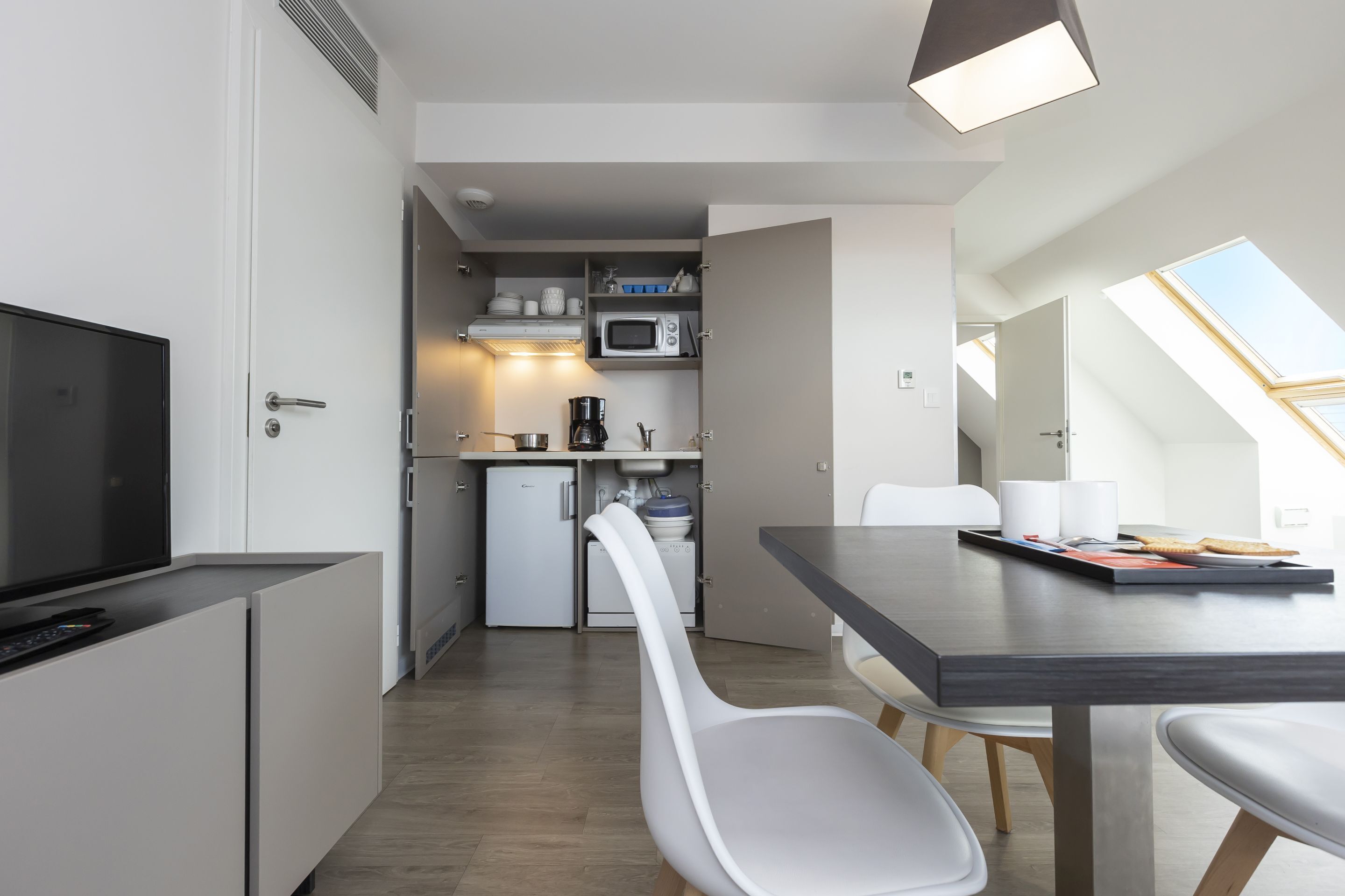 Eine moderne Küche mit Mikrowelle, Kaffeemaschine und kleinem Kühlschrank. Ein Essbereich mit Tisch und Stühlen sowie ein Fernseher auf einem Schrank.