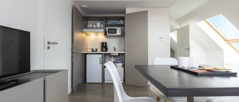 Eine moderne Küche mit Mikrowelle, Kaffeemaschine und kleinem Kühlschrank. Ein Essbereich mit Tisch und Stühlen sowie ein Fernseher auf einem Schrank.
