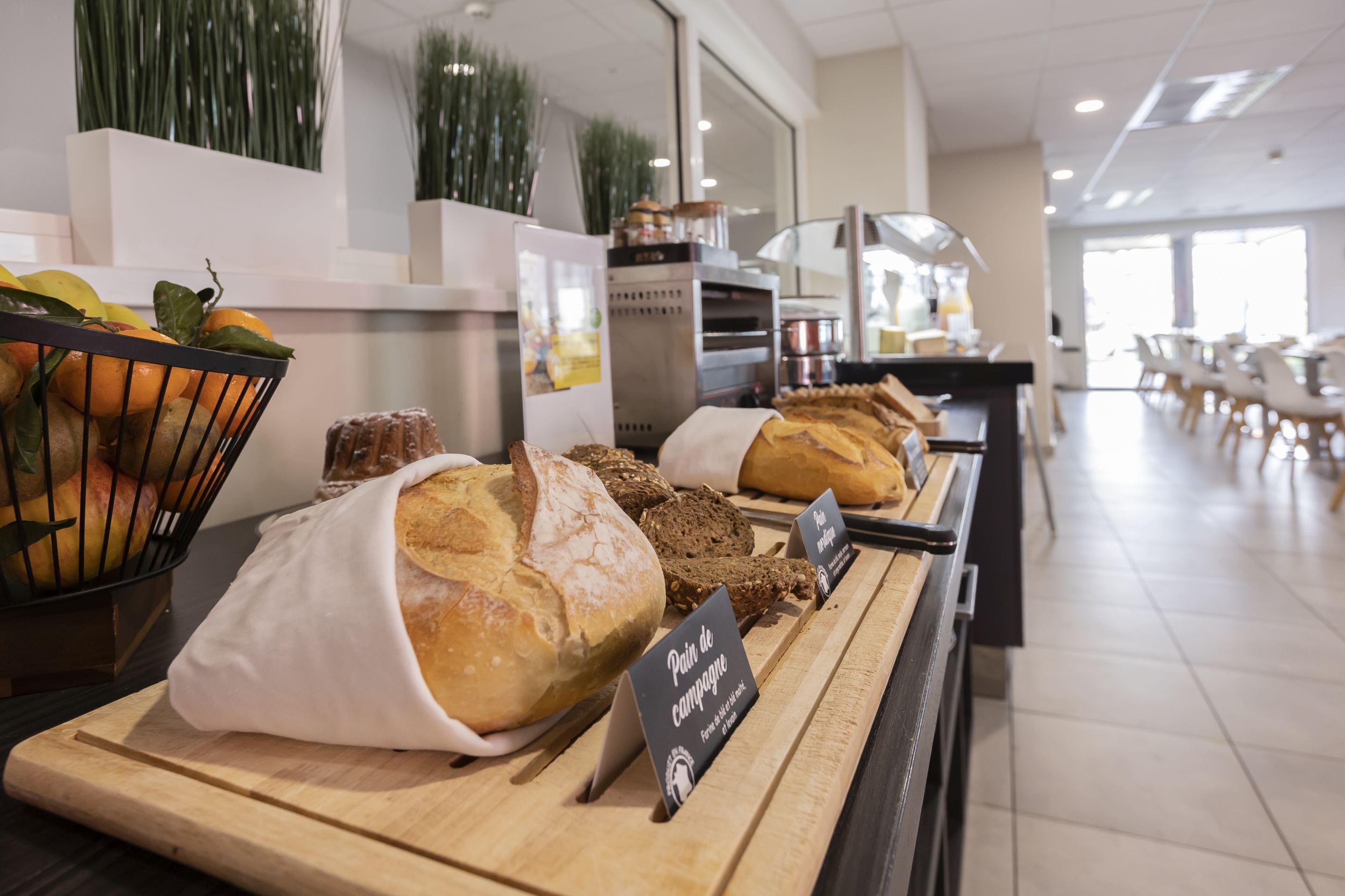 Eine Bäckerauslage mit verschiedenen Broten und Gebäcken, einem Obstkorb und einem Schild, das Pain de campagne anzeigt.
