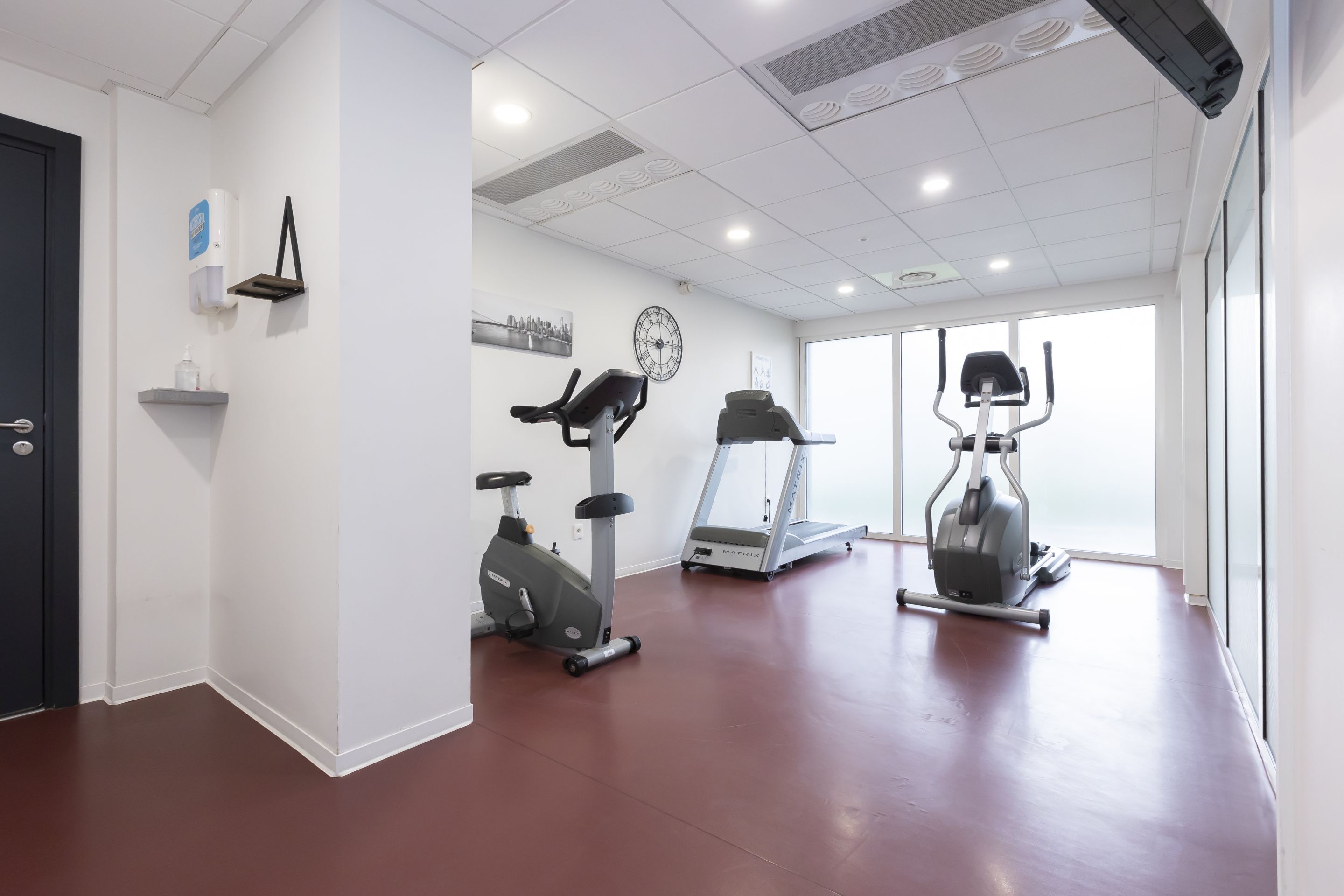 Une salle de sport équipée de tapis de course, de vélos elliptiques et d’une horloge fixée au mur.