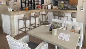 A bar area with a counter, shelves of beverages, and wicker furniture. - Newcastle Studios (Hersonissos)