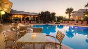 Zona de piscina con sillones de descanso, mesas y un área de estar cubierta.
