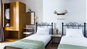A hotel room with two single beds, a wooden wardrobe, a small bedside table with a lamp, and a mirror on the wall. - Newcastle Studios (Hersonissos)