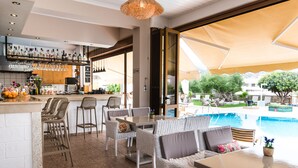 A bar area with a variety of liquor bottles and glasses, wicker furniture, and a view of a swimming pool. - Newcastle Studios (Hersonissos)