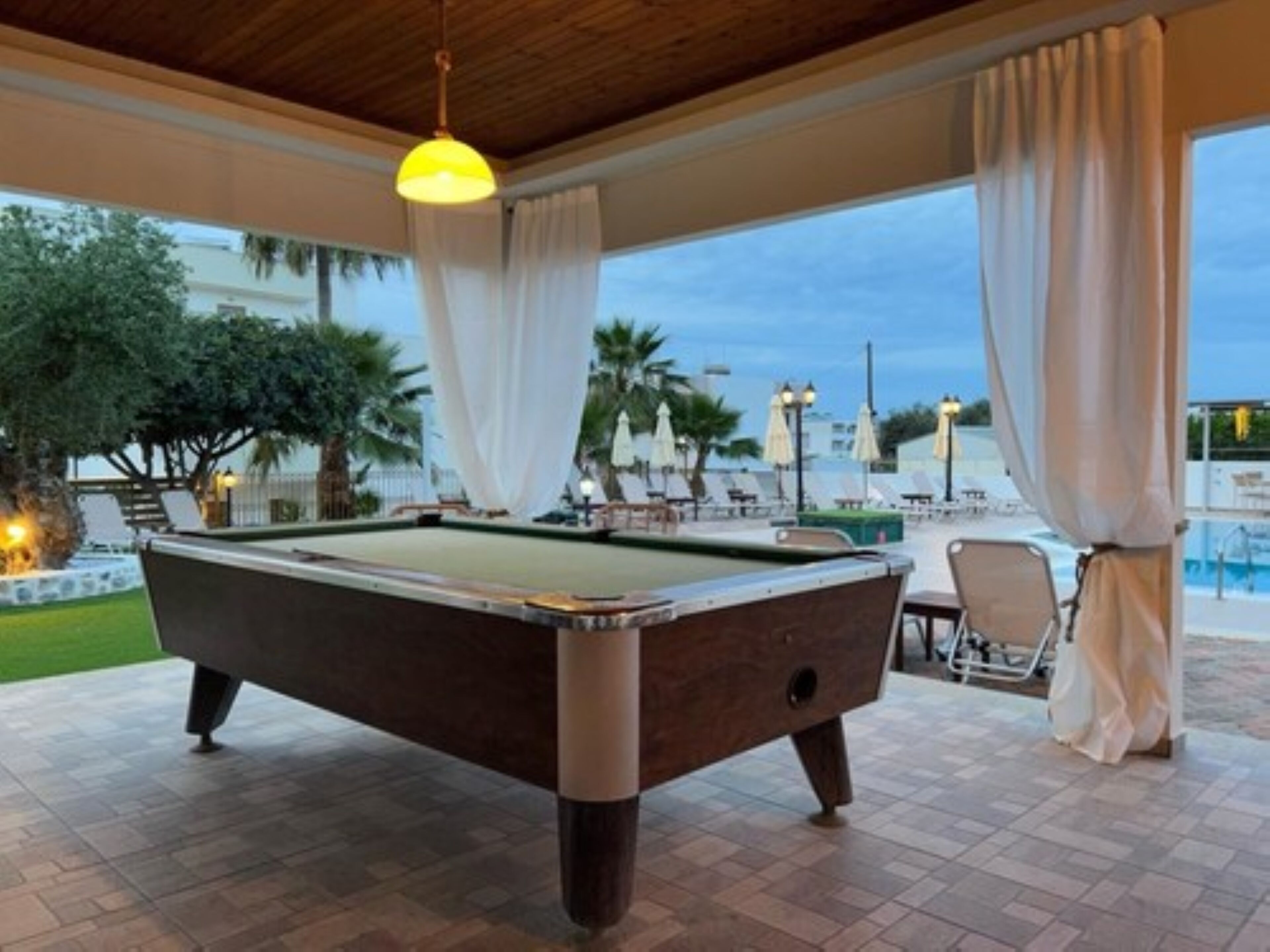 A pool table in an outdoor area with a view of a pool and palm trees.