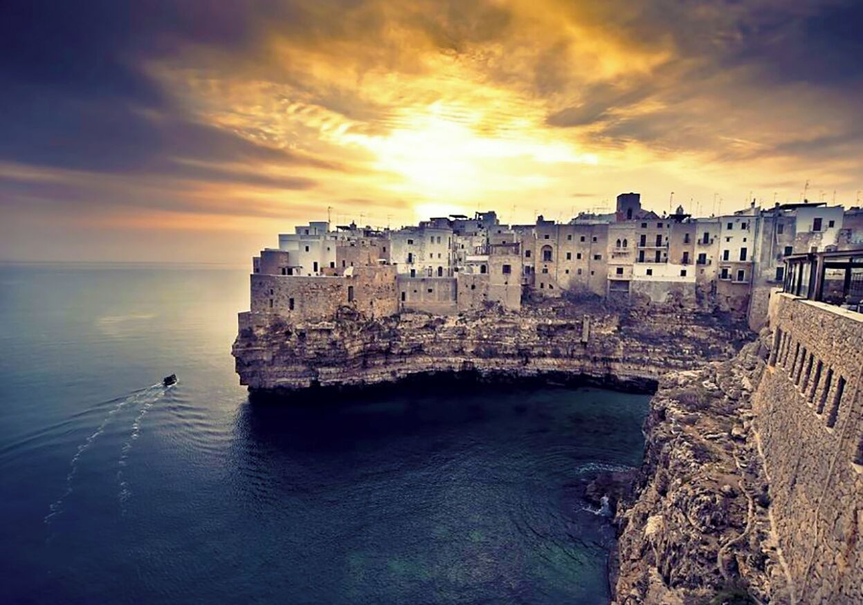 Un pueblo costero con edificios a lo largo de un acantilado con vistas al mar, cielo despejado y un atardecer.