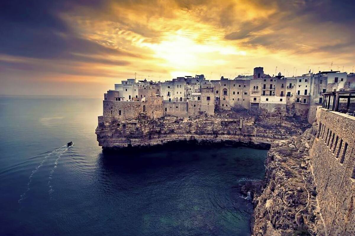 Une ville côtière avec des bâtiments qui s’étendent le long d’une falaise surplombant la mer, un ciel dégagé et un coucher de soleil.