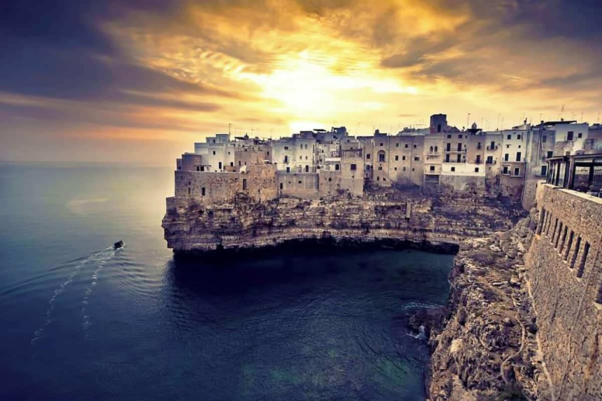 A coastal town with buildings along a cliff overlooking the sea, a clear sky, and a sunset.