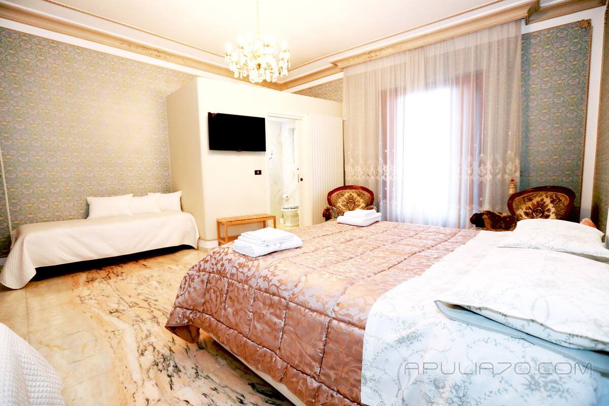 Une chambre d’hôtel avec un grand lit, un téléviseur fixé au mur et un lustre.