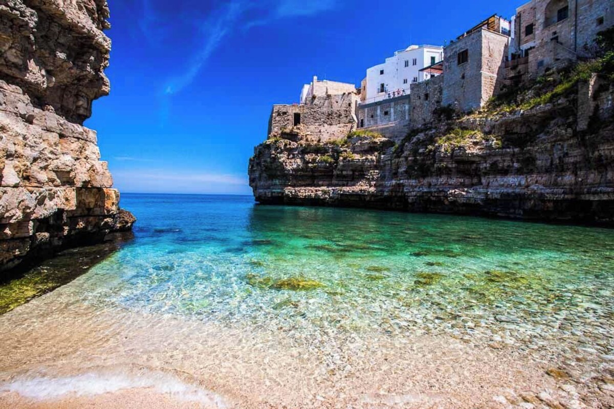 Un pueblo costero con aguas cristalinas, edificios de piedra y un litoral rocoso.